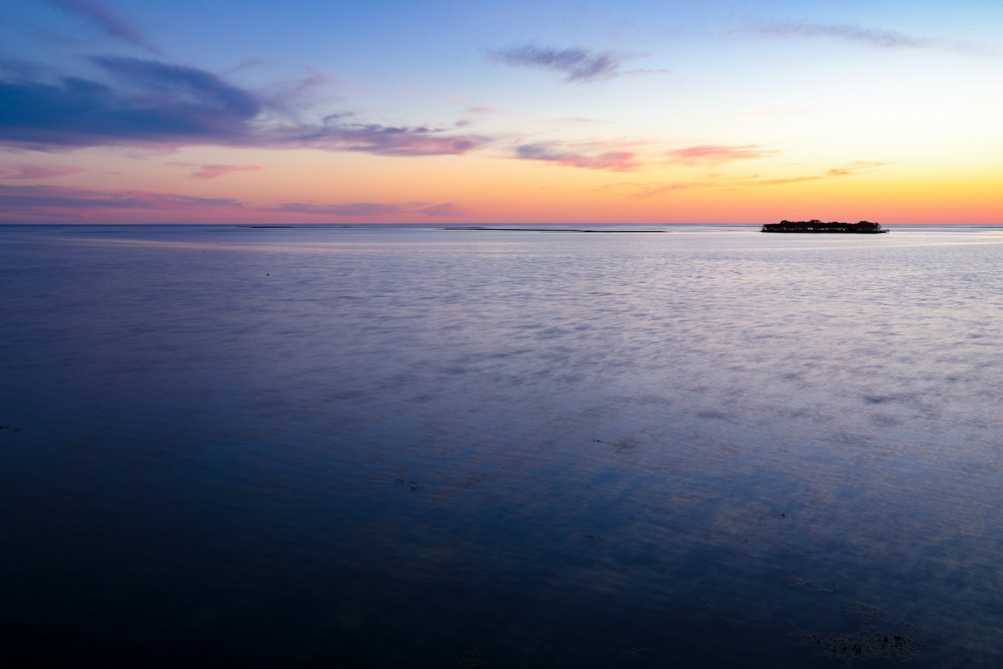 Calm ocean water under a twilight sky with distant land.